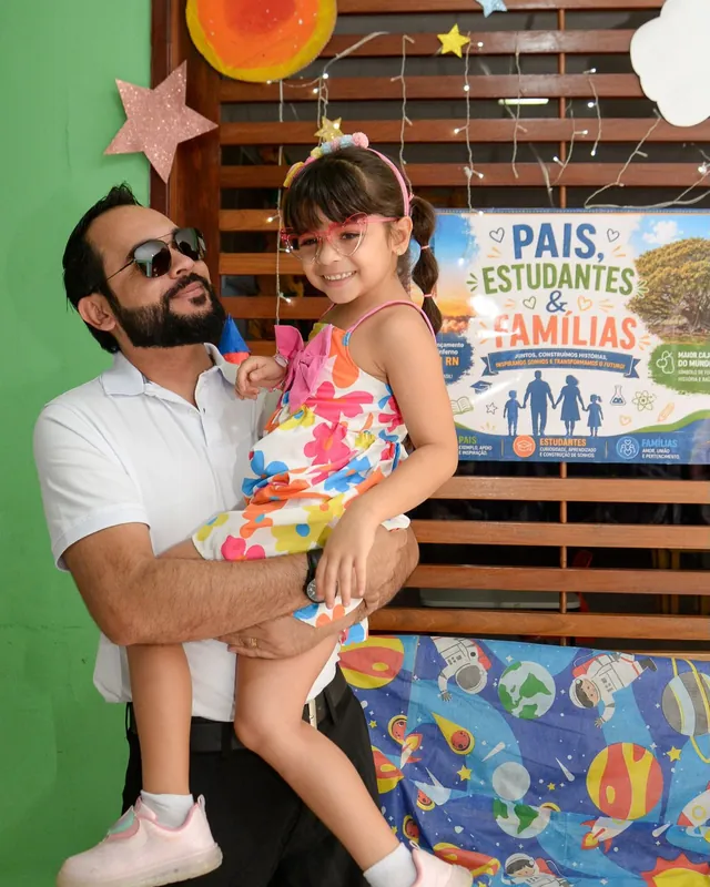 Pai segurando a filha no colo, os dois sorrindo, no encontro de pais, estudantes e famílias da CaHsi