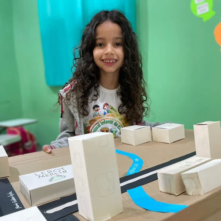 Aluna da CaHsi sorrindo ao lado da maquete do bairro que a turma construiu